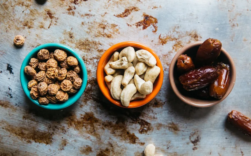 Drei Schälchen mit Erdmandeln, Cashewkernen und Datteln auf einem Blech